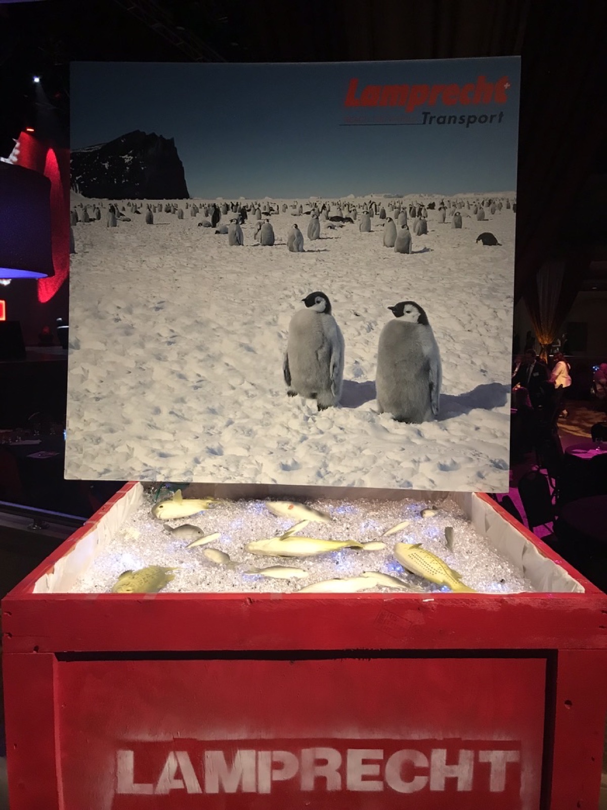 Lamprecht Transport event installation with a penguin photograph above a red branded crate.